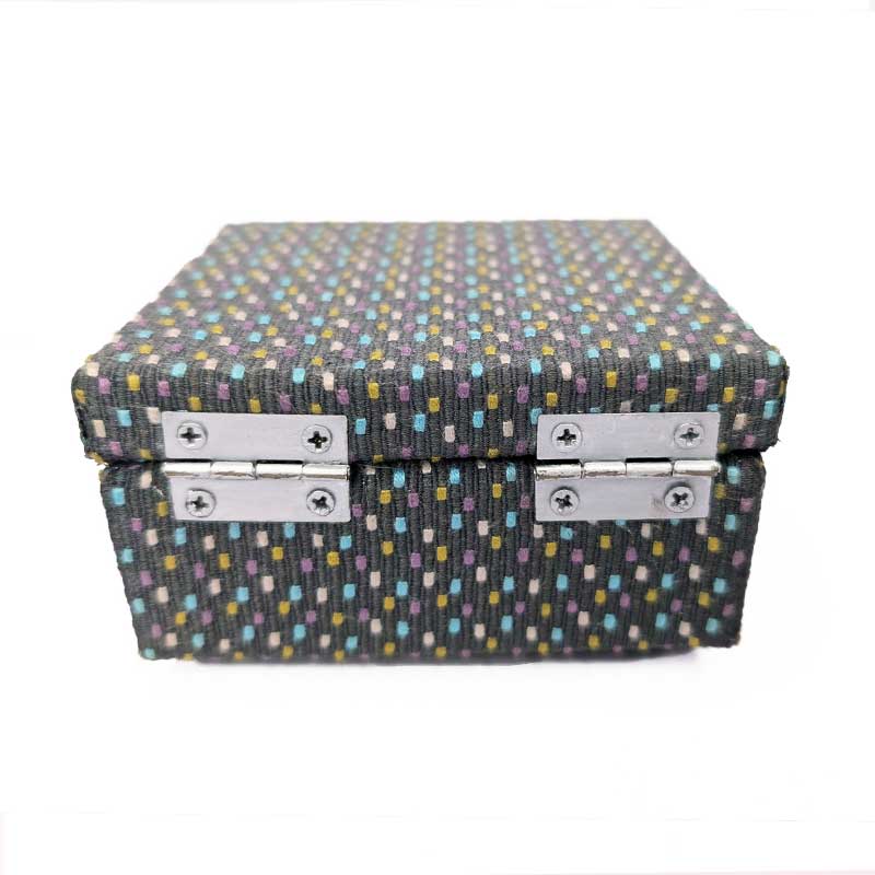 A rectangular dice storage box with a textured fabric cover featuring a multicolor dotted pattern on a dark gray background, secured with two silver metal latches on the back, set against a plain white background.