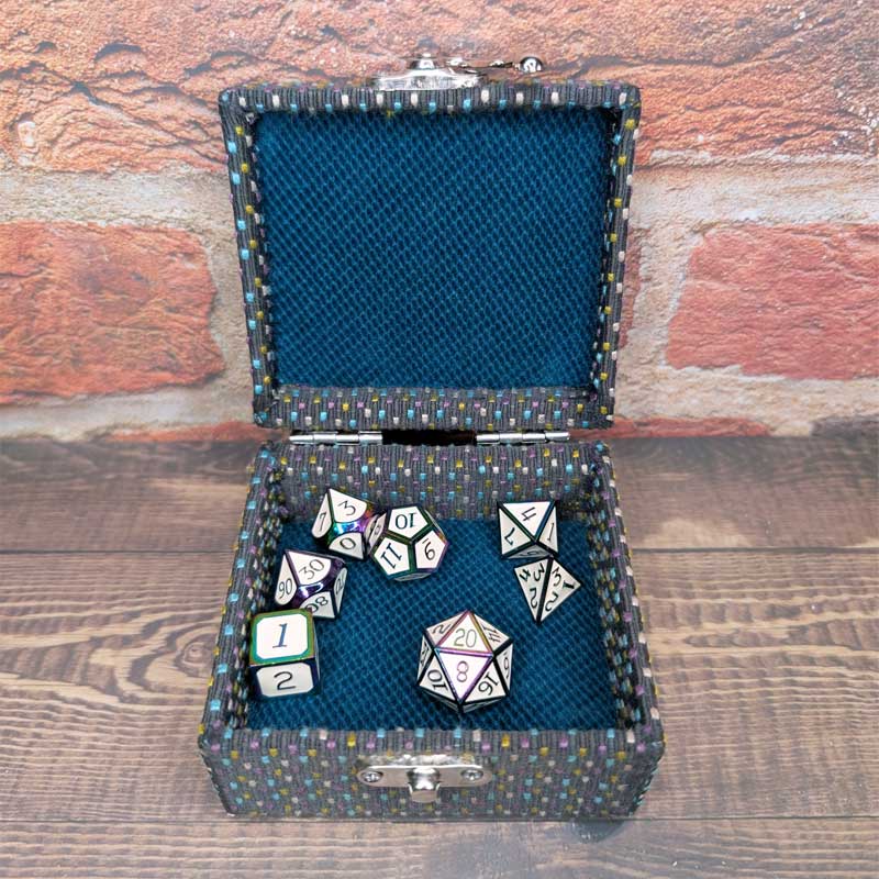 An open dice storage case with a dark blue mesh interior, containing several white and multicolored polyhedral RPG dice, set against a rustic brick and wood background.