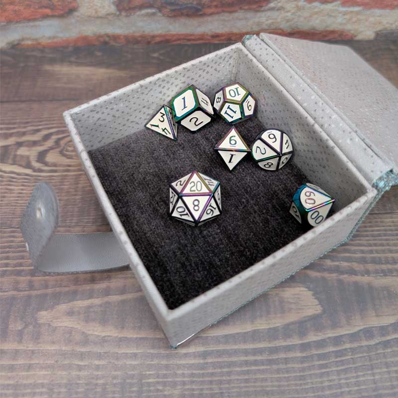 A 7-piece polyhedral gaming dice set displayed inside an open gray textured dice storage box with a dark plush lining, set on a wooden tabletop.