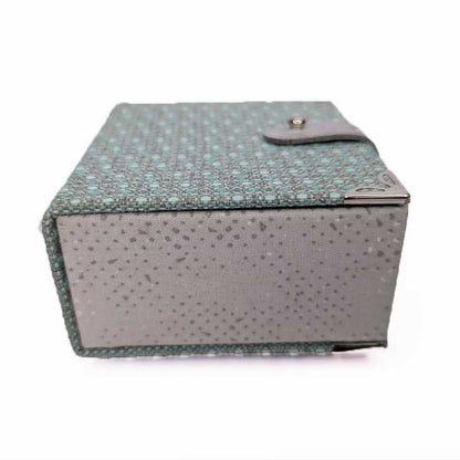 A rectangular dice box with a textured, speckled pattern in teal and gray, featuring a small gray leather strap closure on the lid, set against a plain white background.