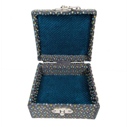 An open square dice box with a dark blue velvet-lined interior and a patterned exterior featuring small multicolored dots on a dark charcoal base, with silver-tone metal clasp hardware.
